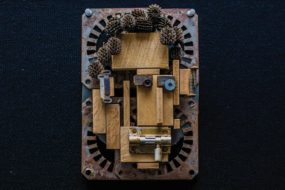 Abstract commissioned sculpture of a face constructed from wood blocks, metal hardware, and pinecones on a rusty metal base